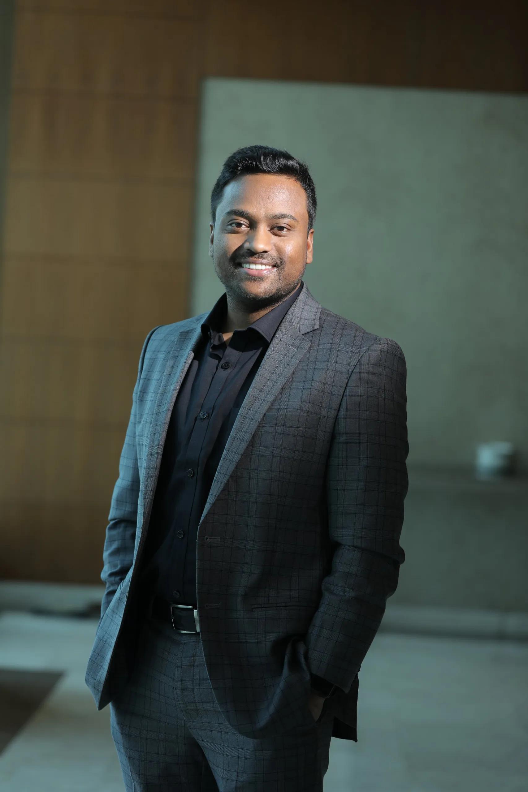 Keshave Lal, business coach, smiling in a grey checked suit and black shirt