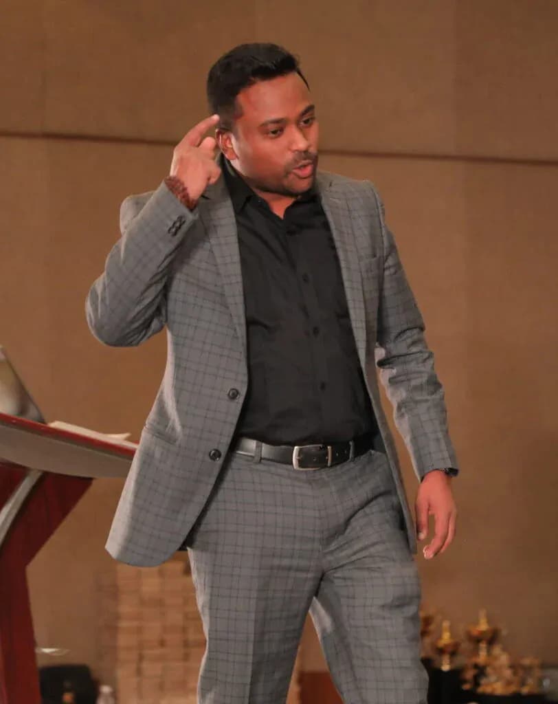 Keshave Lal speaking on stage in a grey suit